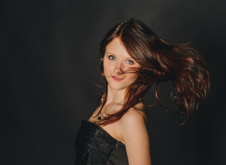 Naklejka premium beautiful young woman with red hair and blue eyes on dark background with flying hair