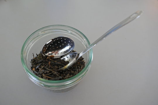 Trockener gr&uuml;ner Tee mit einem silbernen L&ouml;ffel mit Teefilter in einem Aufbewahrungsglas
