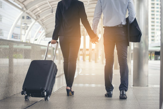 Asian Business man and woman  Dragging suitcase luggage bag,walking to passenger boarding in Airport,travel to work. Couple of love wearing black suit pull trolley bag. Business travel concept