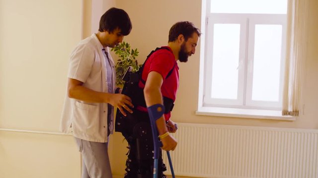 Young disable man walking in the robotic exoskeleton in the rehabilitation clinic. Side view