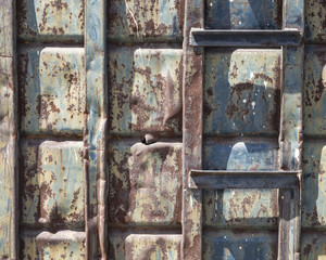 A detailed close-up of a dumpsterâs weathered surface texture, structural geometry, and varying muted tones of blue, yellow, and rusty red.