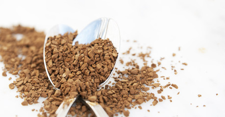 Pile of instant coffee grains on silver spoon, over marbble surface. Caffiene drink. Banner.