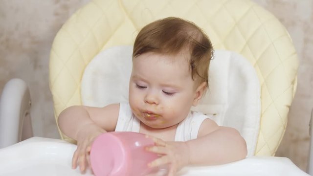 Mom feeds baby from spoonful of porridge. Baby sits in kitchen at table and eats