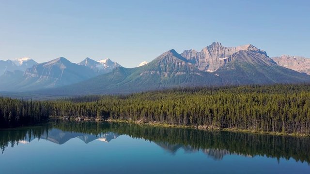 Aerial shot above lake next to road with mountains and forest while sunset in Rocky Mountains in Canada