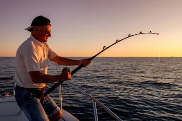 Fototapeten Angler, die bei Sonnenuntergang vom Boot aus auf dem Meer fischen © Federico Rostagno