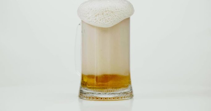 Pouring mug of beer with foam running out isolated