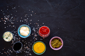 Set of sauces. Ketchup, mayonnaise, mustard, soy sauce, barbecue sauce, pesto, mustard, sour with greenery on black background top view copy space
