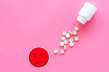 Illness. Drug intake. Pills falling out of jar near sad face emoji on pink background top view copy space