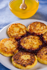 Cottage cheese pancakes on blue napkin. Traditional Ukrainian dish - syrniki with jam on a wooden background. Pancakes with cottage cheese on a white plate with honey