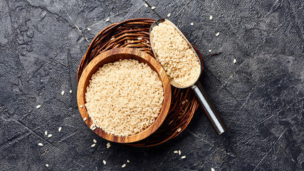 White rice in wooden bowl on black background. Top view of grains.