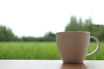 Woman holding hot coffee cup in the morning green meadow background.