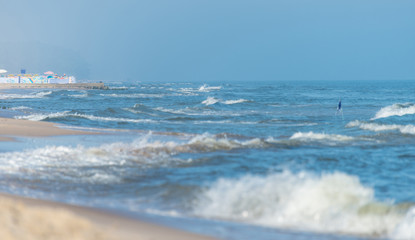 Rough waves on a beautiful blue sea on a summer, sunny and windy day. Protruding warning flags from the sea.