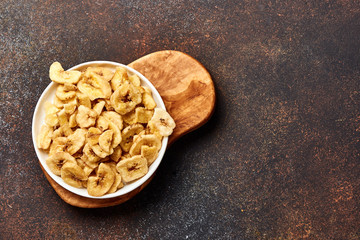 Dried banana slices on brown background. Top view of banana crunchies.
