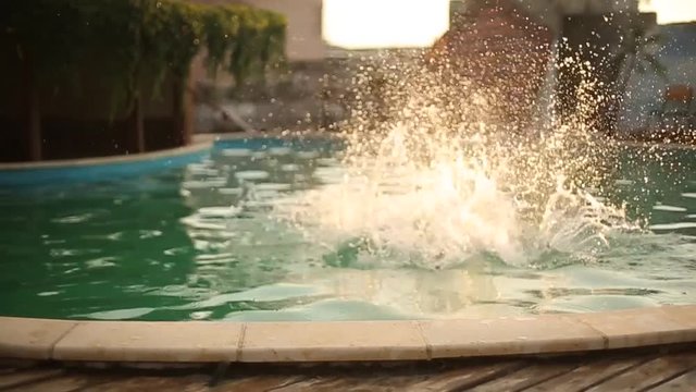 Young woman on summer vacation jumping into clear blue pool water for refreshment on hot sunny day with splashes and spray in slow motion. Girl in blue bikini diving into pool in empty luxury resort.
