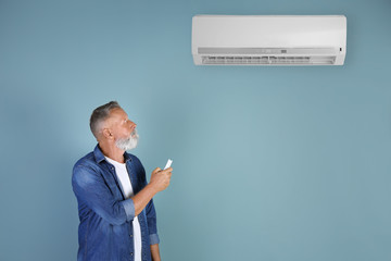 Senior man with air conditioner remote control on color background