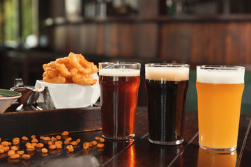 Glasses of tasty beer and snacks on wooden table in bar
