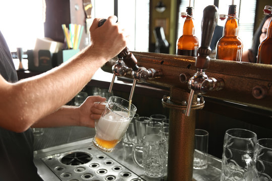 Bartender pouring beer from tap into glass in bar, closeup