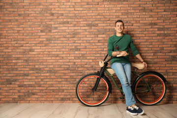Fototapeta premium Portrait of handsome young man with bicycle near brick wall