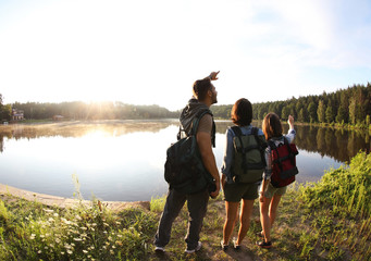 Young friends on shore of beautiful lake, wide-angle lens effect. Camping season