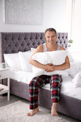 Happy man with soft pillow sitting on bed at home