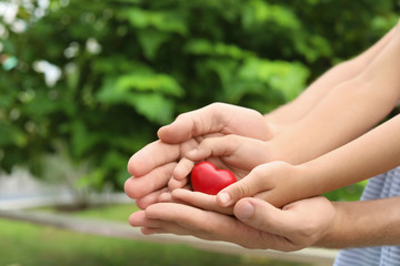 Family holding small red heart in hands together outdoors, closeup