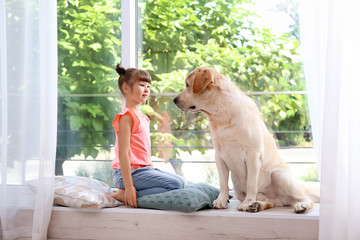 Adorable yellow labrador retriever and little girl near window at home