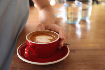 Woman with cup of fresh aromatic coffee at table, closeup