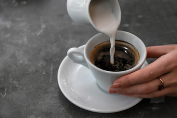 Woman adding milk to fresh aromatic coffee at table, closeup