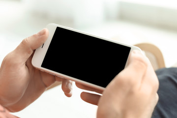 Man holding mobile phone with blank screen on blurred background, closeup. Mockup for design