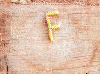 F letter done with pasta fusilli on a wooden chopping board