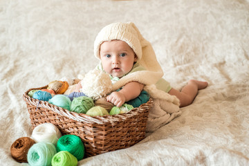 A cute baby lies on a basket with tangles of knitting threads. Hendmeid of multi-colored threads