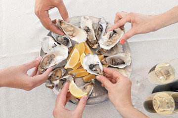 Top view of people with fresh oysters at table, focus on hands
