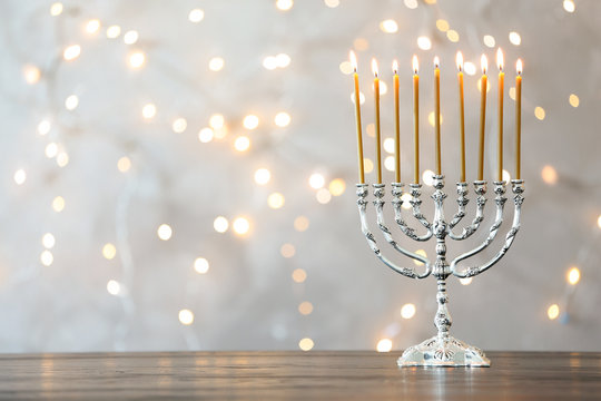 Hanukkah menorah with candles on table against blurred lights