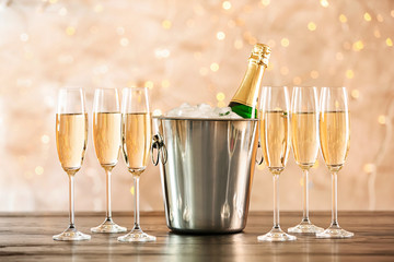 Glasses with champagne and bottle in bucket on table against blurred lights