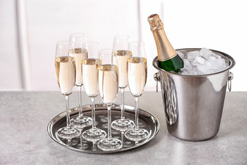Glasses with champagne and bottle in bucket on table indoors