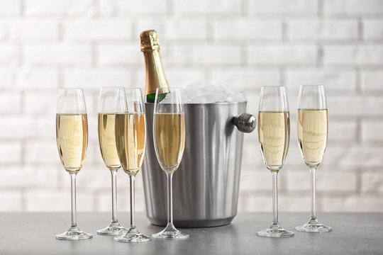 Glasses with champagne and bottle in bucket on table against brick wall