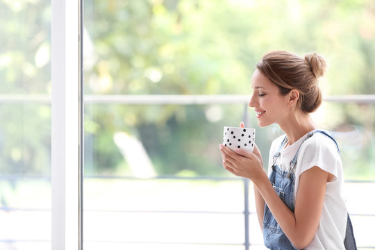 Young woman with cup of aromatic coffee near window at home