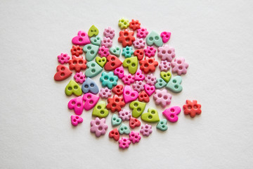 Mixed coloured bright buttons. Colored buttons in the shape of heart. Button plastic colorful on white background and copy space. Beautiful color buttons. Sewing buttons.  Many color plastic.