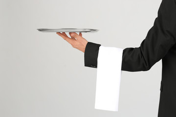 Waiter holding metal tray on light background