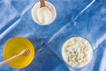 Milk products and honey with wooden cutlery. Cottage cheese, sour cream, cream on a blue napkin top view. Different natural products for vegan. Healthy food