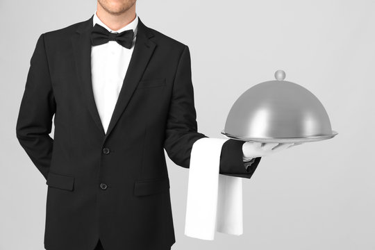 Waiter holding metal tray with lid on light background