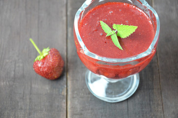 Summer dessert, panna cotta or yogurt or pudding or jam with strawberrieswith strawberries decorated with mint leaves. On a brown wooden table, bright sunlight. Copy space. close up