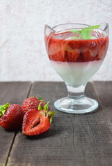 Summer dessert, panna cotta or yogurt or pudding or jam with strawberrieswith strawberries decorated with mint leaves. On a brown wooden table, bright sunlight. Copy space. close up