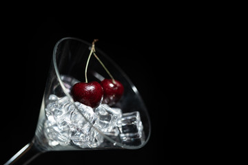 Fototapeta na wymiar Close up view of cherry in a martini glass among ice in black background.