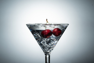 Close up view of splash water with falling cherry in a martini glass among ice in white background.