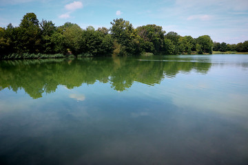 Garching, Bavaria - Beautiful summer view of Garchinger See, lake near Munich, with calm blue waters reflecting wood, sky and clouds