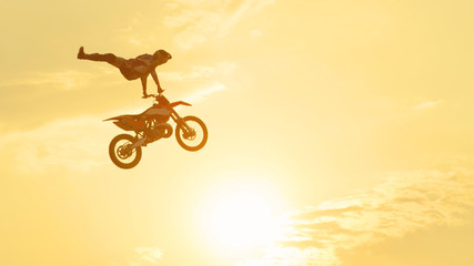 Pro freestyle motocross biker jumping extreme trick over sunset sky