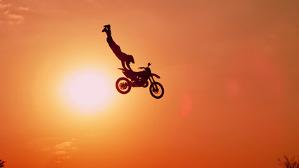 Pro motocross biker jumping no hands superman against sunset sky