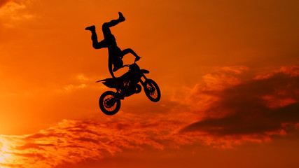 Extreme pro motocross biker jumping freestyle trick over the sun