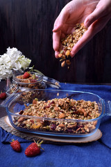 Female hands are strewing granola into the glass baking dish